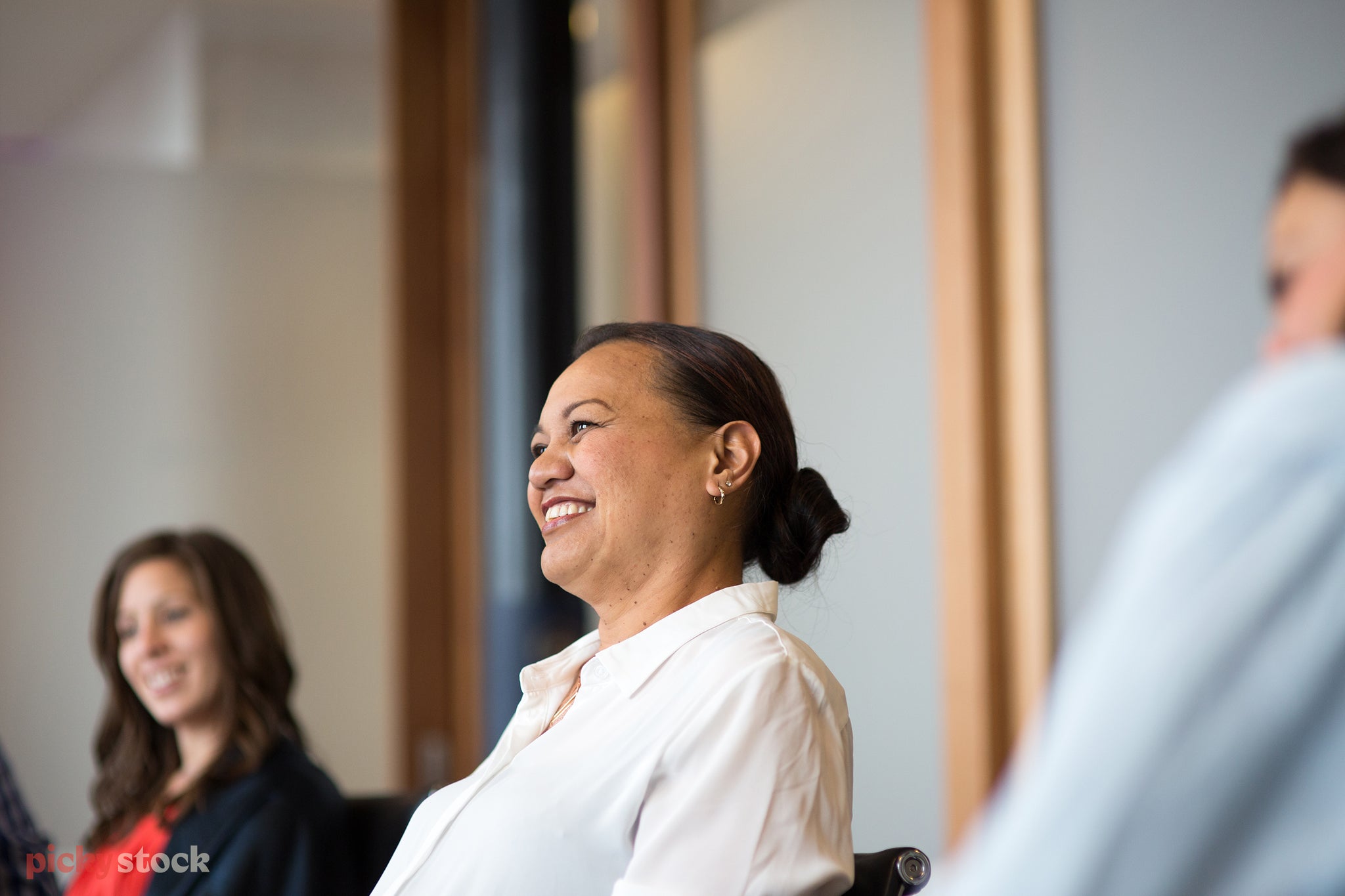 Observational image of Māori lady laughing off into the distance in a board room meeting. Her colleagues look on in the same direction. 