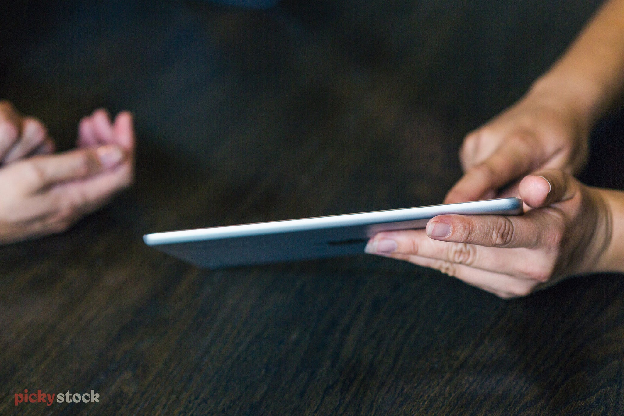 Close up of hands holding iPad or other tablet device. Another hand points, showing the holder what to do.