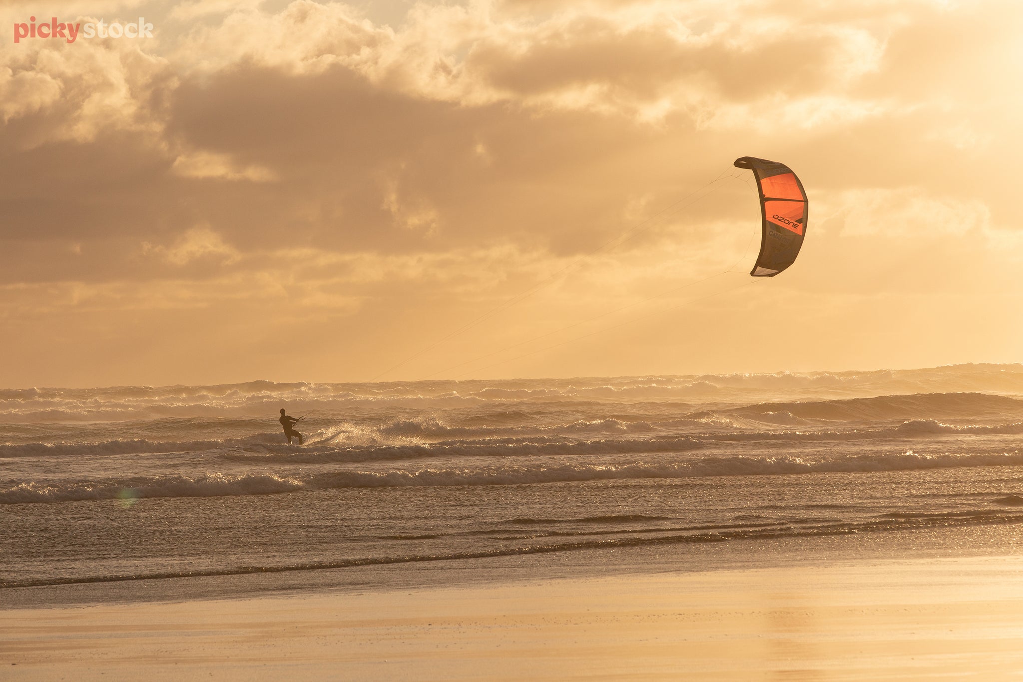 Kite-surfer holds orange kite out to the right, as the ride little waves at golden hour. 