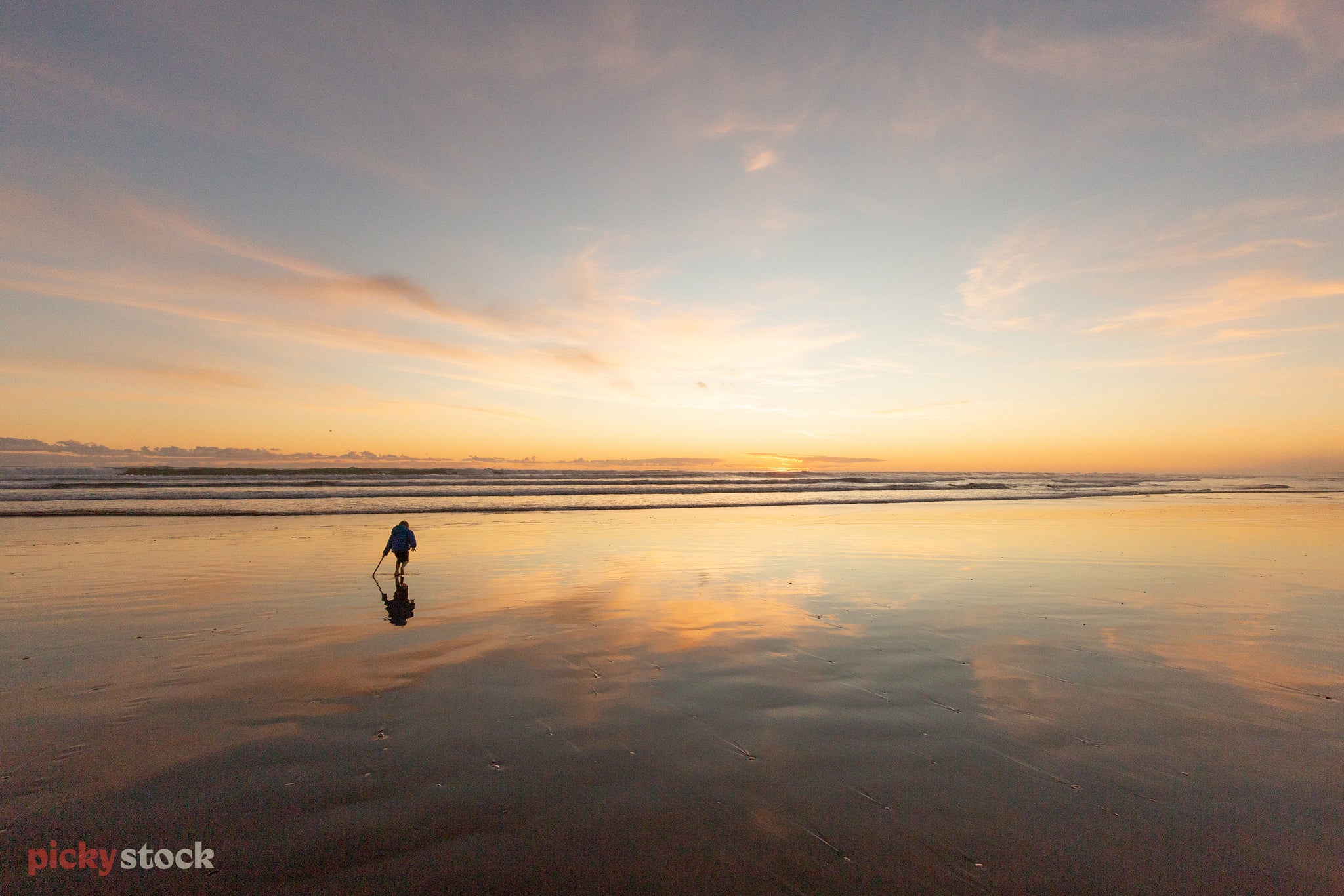 Silhouette of a young boy drawing on the sand with a stick, it's sunset and the light is reflected in the sea and sand. 