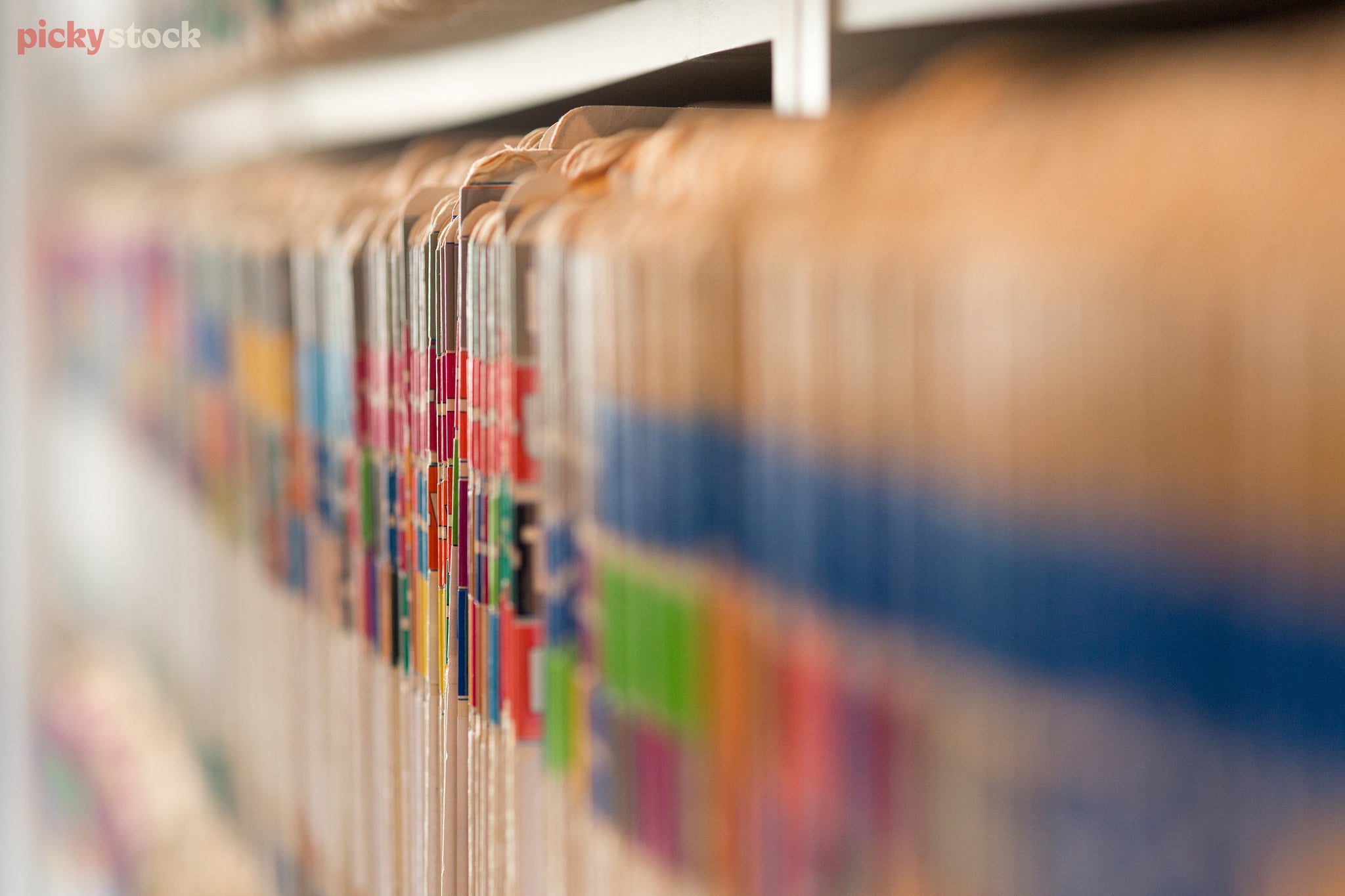 Looking along rows of old medical files, with colourful tags, all organised in a shelving unit in a practice. 
