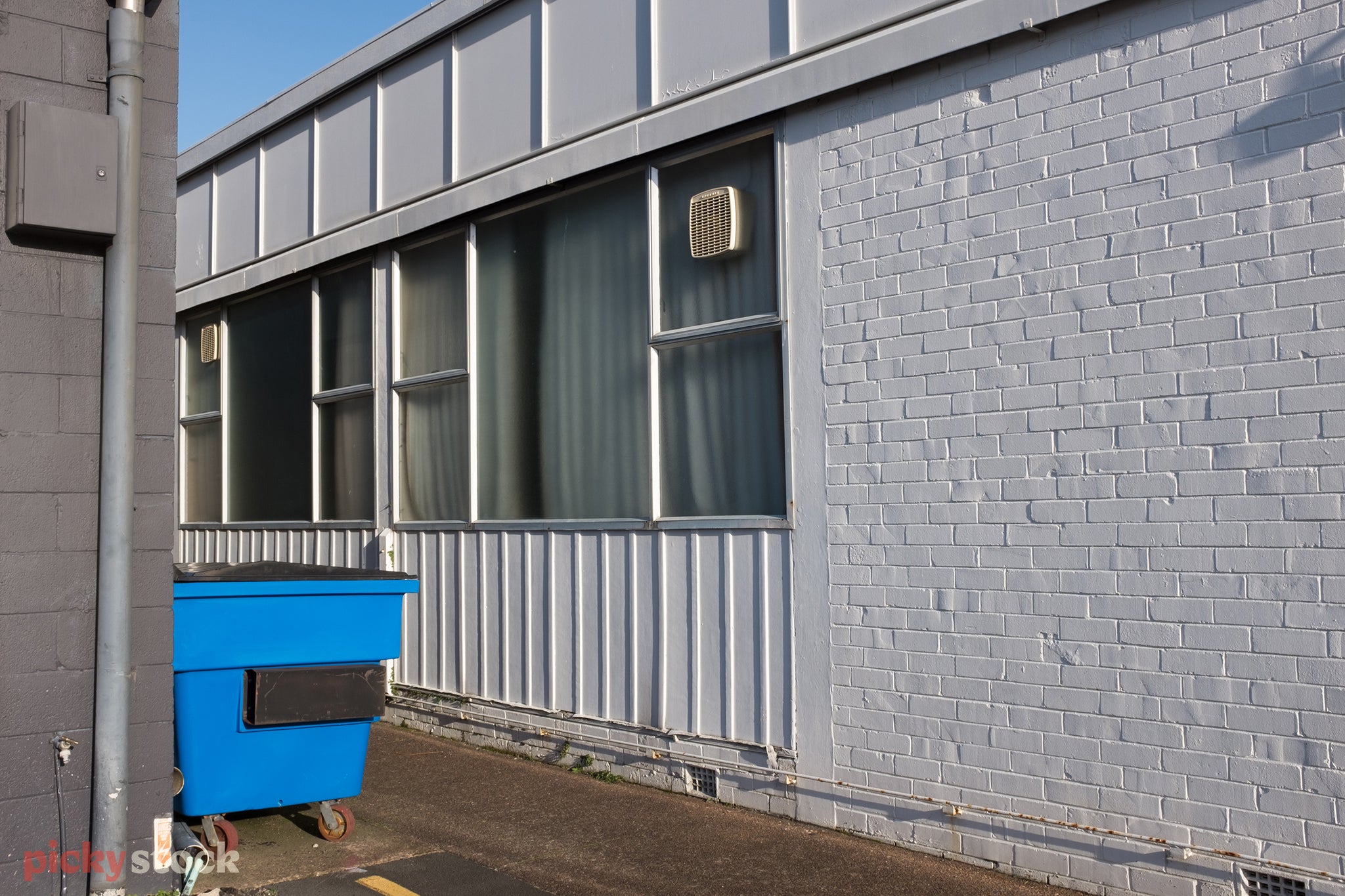 Bright blue skip bin, sits tucked against a white painted old industrial block.