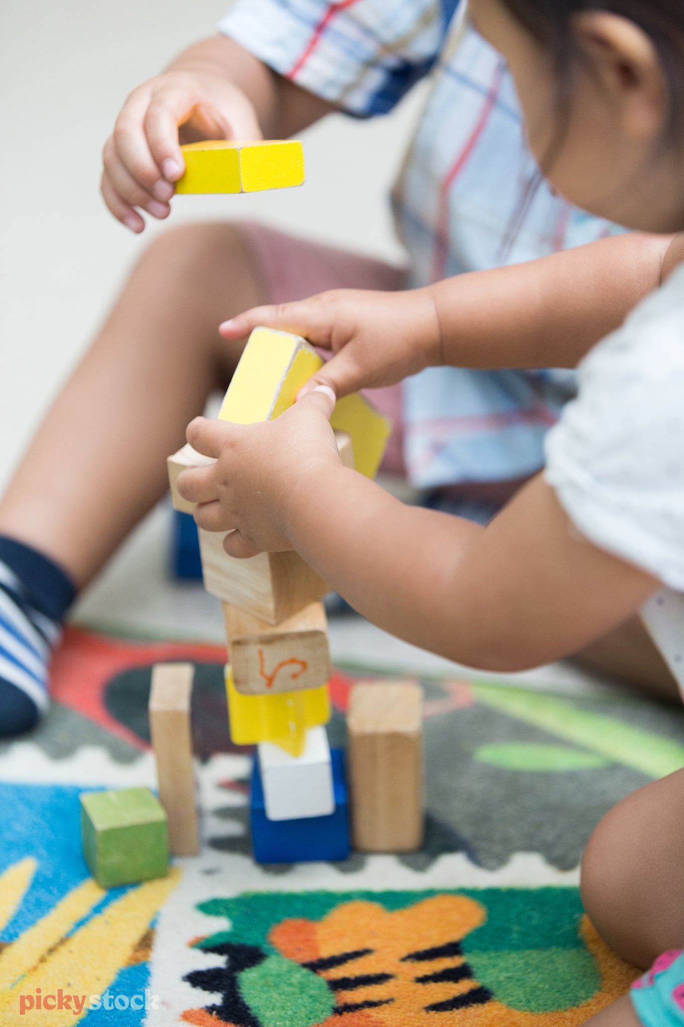 Toddlers play with building blocks, stacking the colourfull basic blocks on top of each other to form a little tower. 