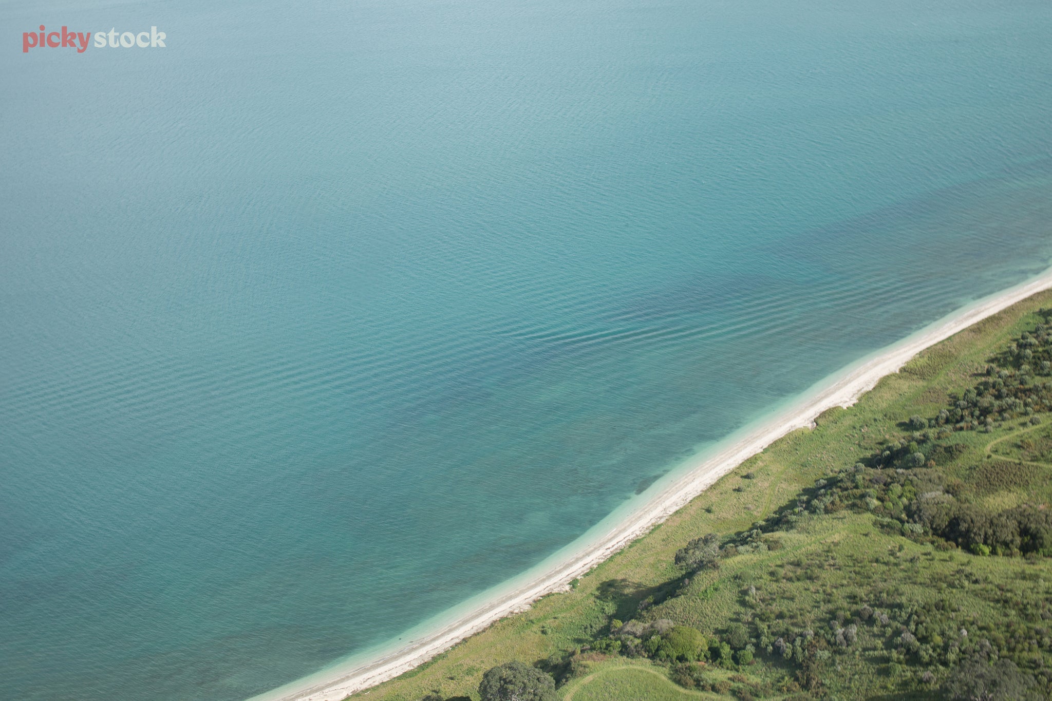 High angle aerial image of coastline and sea. The sea hits the coast towards the bottom right corner, where lots of native bush and greenry can be seen. 