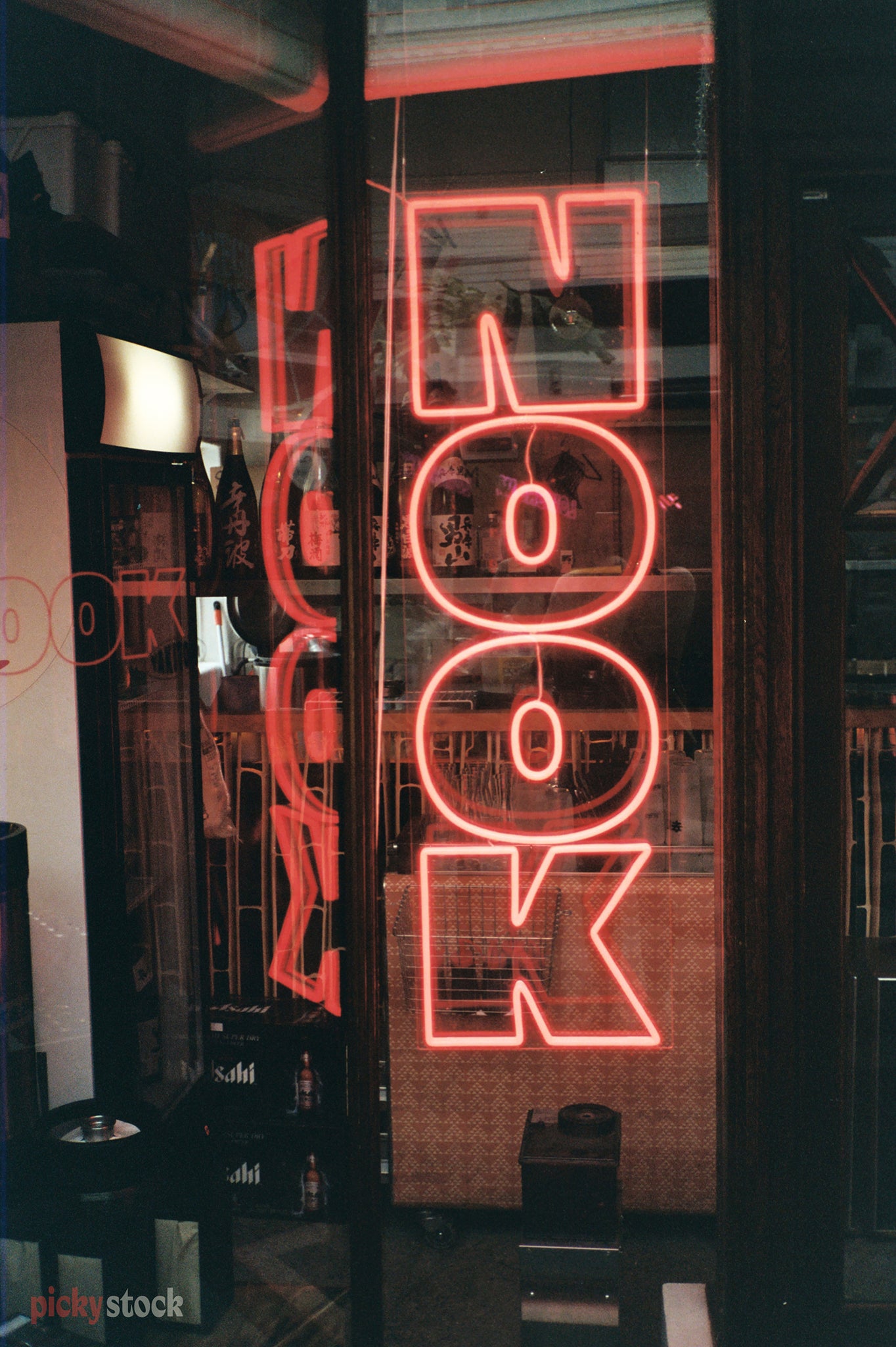 A neon red sign with the word "NOOK" hangs in the window of a shop on Karangahape Road, Auckland Central. The lights reflect off the glass. 