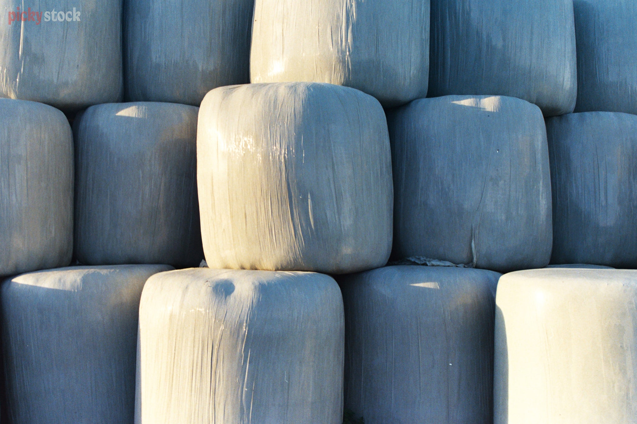 Grey hay bales stacked up after the harvest. The light hits the large bails.