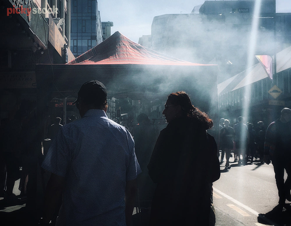 Candid image walking down the pavement behind an unrecognisable couple. They're heading towards a food market, the smoke from the food cooking distorts the view.