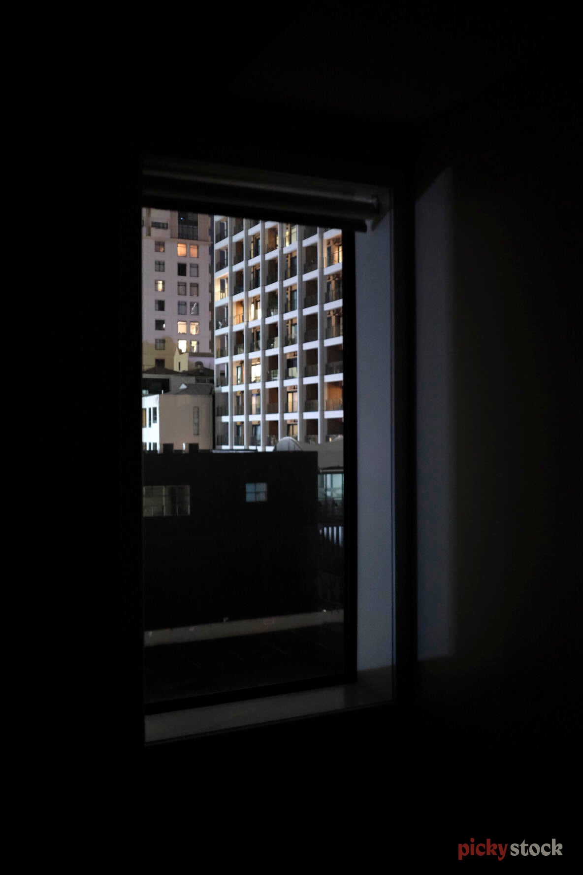 Looking out from the darkness of an old apartment block, through to another apartment block, Auckland. The majority of the image is black, as it's later in the day. With glints of light striking the other apartment block in the distance. 