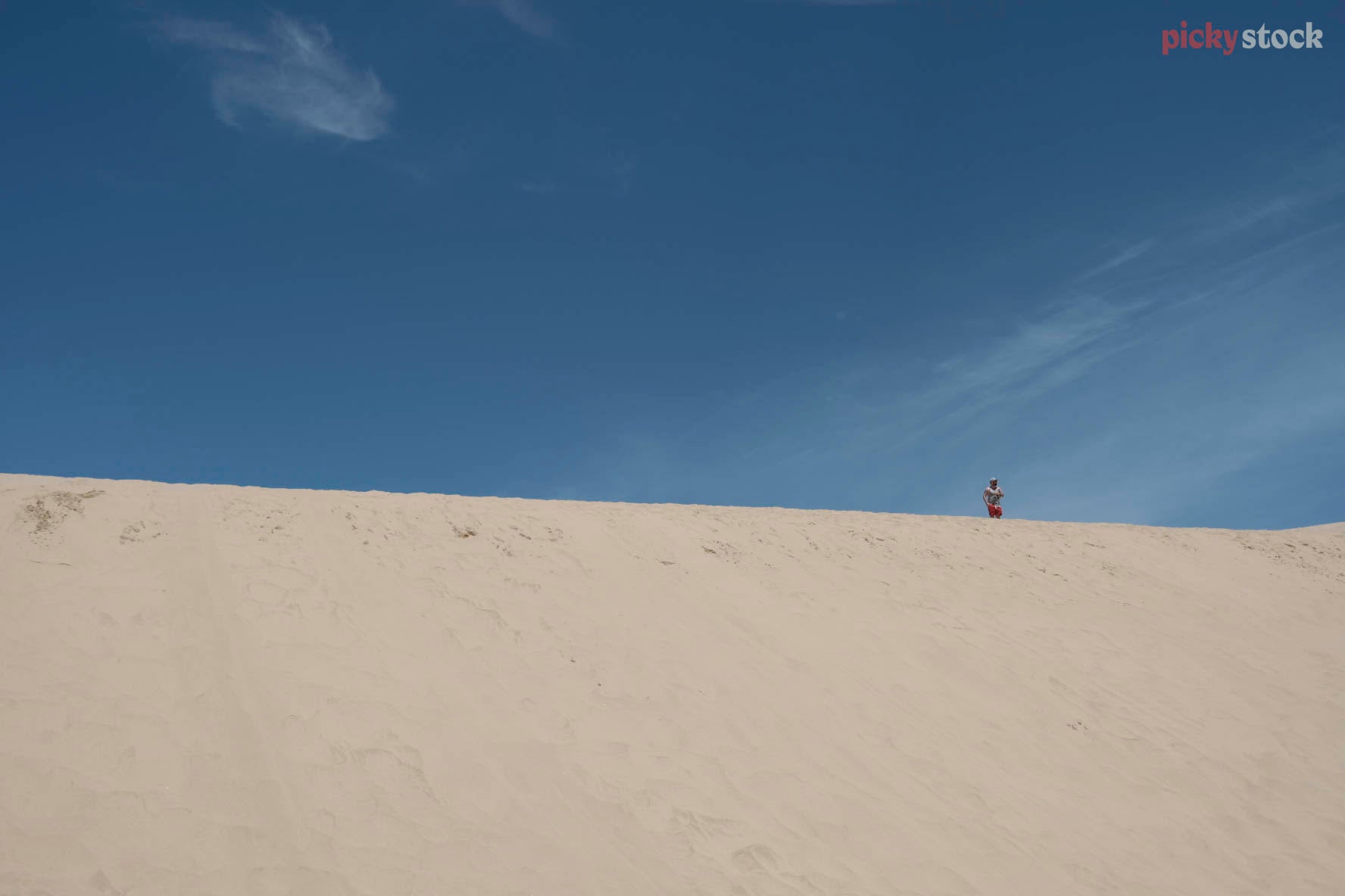 A graphic composition where one giant sanddune cuts across the image from left to right. The bottom half of the image is covered in golden sand. The top half blue skies. 