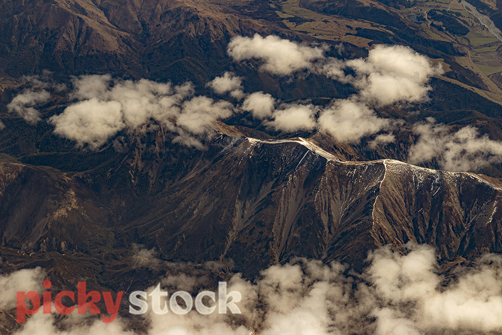 The ridge of the Southern Alps break through some soft white clouds.