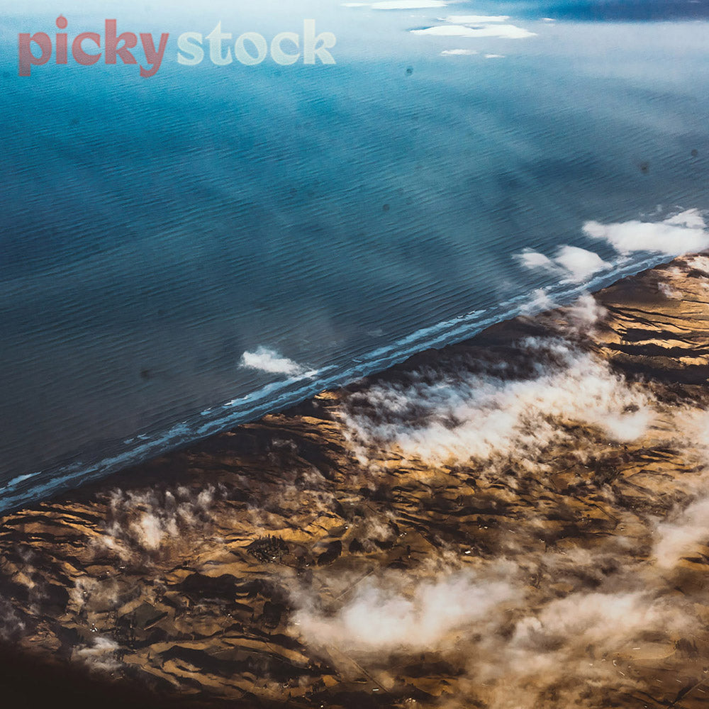 Graphic aerial shot of land meeting sea on the coast. the small swell rolling in and clouds see rolling over the land.