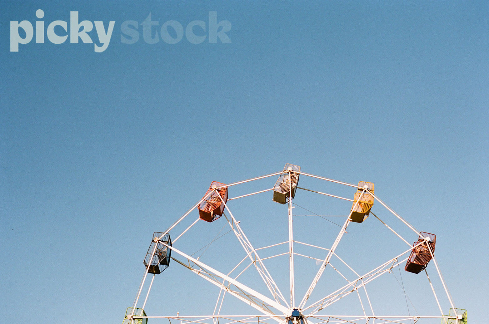 Close up of a ferris wheel in local park. Background is a soft blue, no clouds in the sky. 
