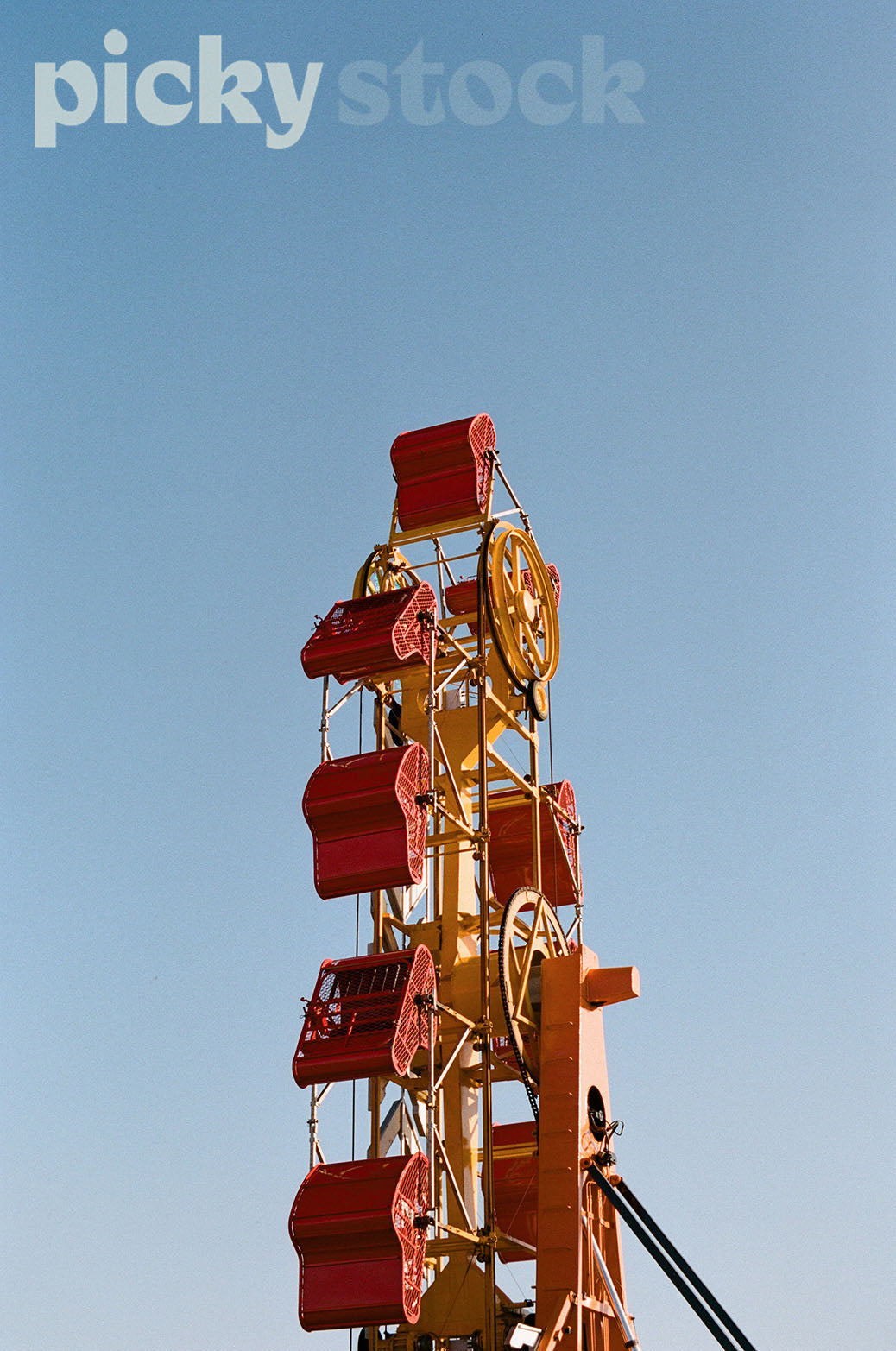 Blue, cloudless sky. Close up of theme park ride. With red carts, with yellow base.