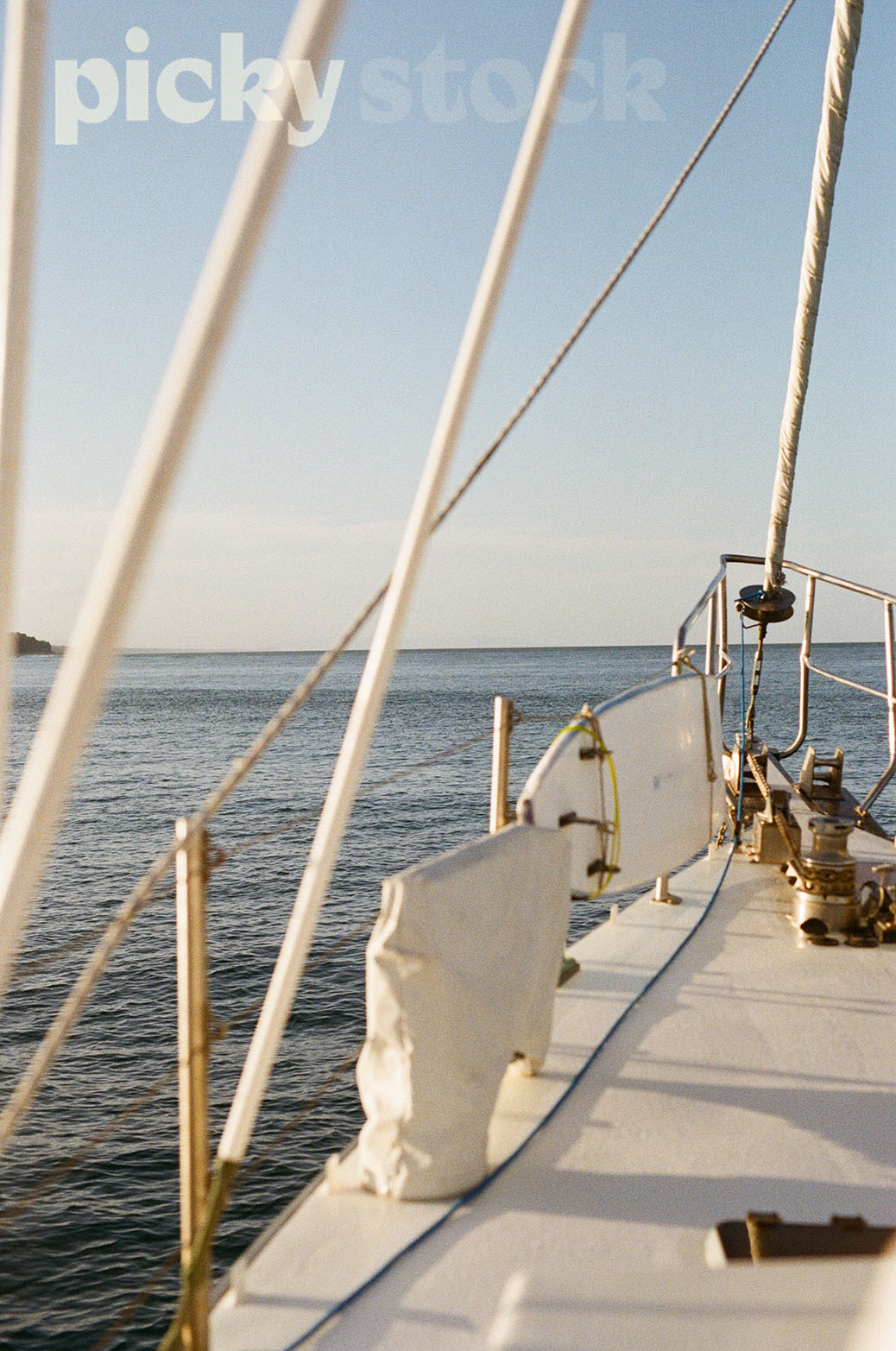 Portrait shot of the front of the boat, bow. View of the ocean looking to the horizon. Blue ocean, with soft blue sky. 