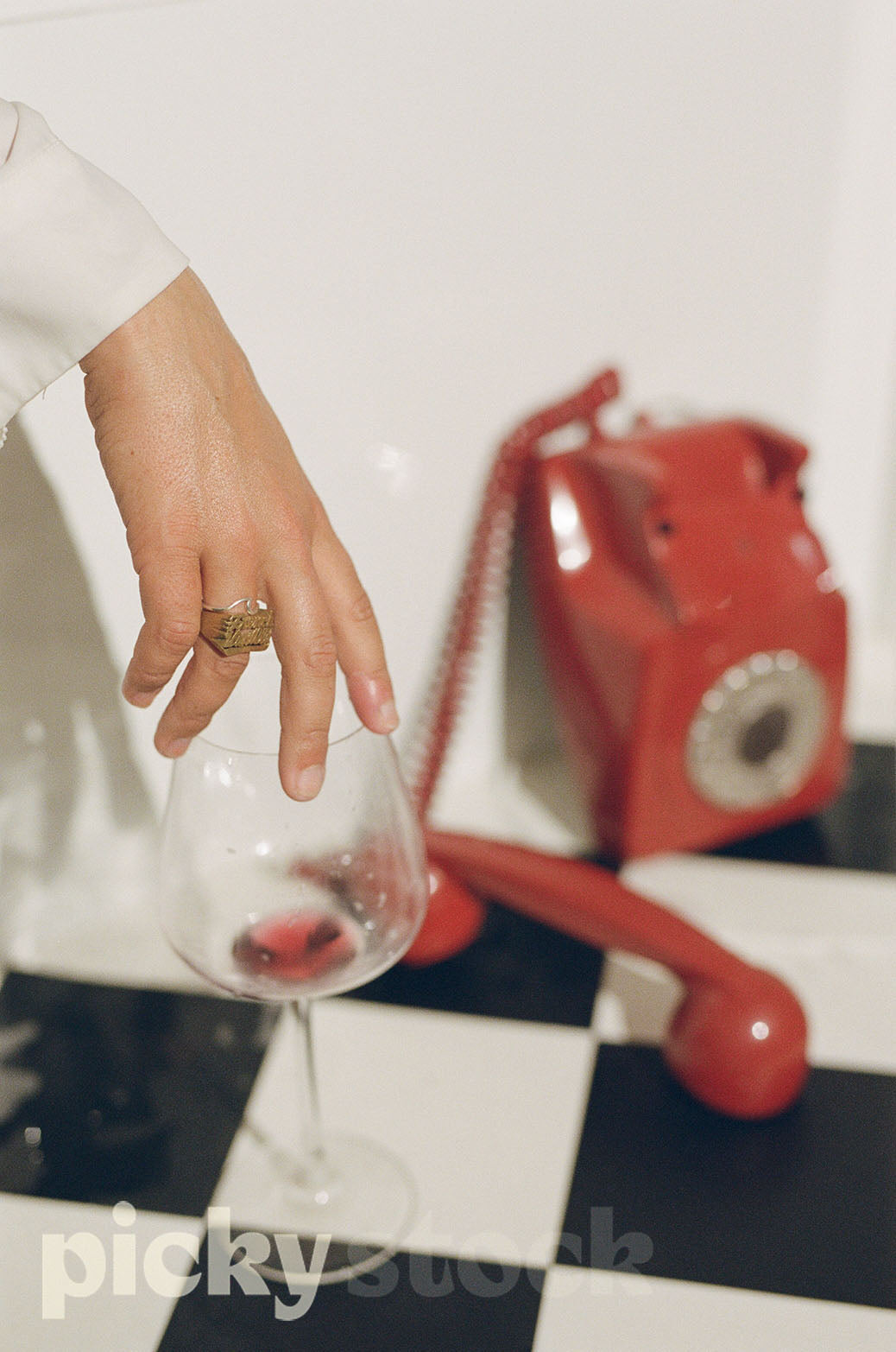 Female hand picking up red wine glass from rim. With red vintage phone in background. Items sitting on a black and white checkerboard floor