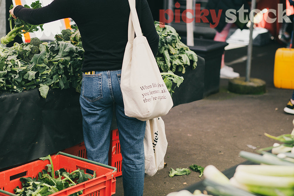 Young woman shopping for produce farmers market with reusable tote bags buying brocolli.