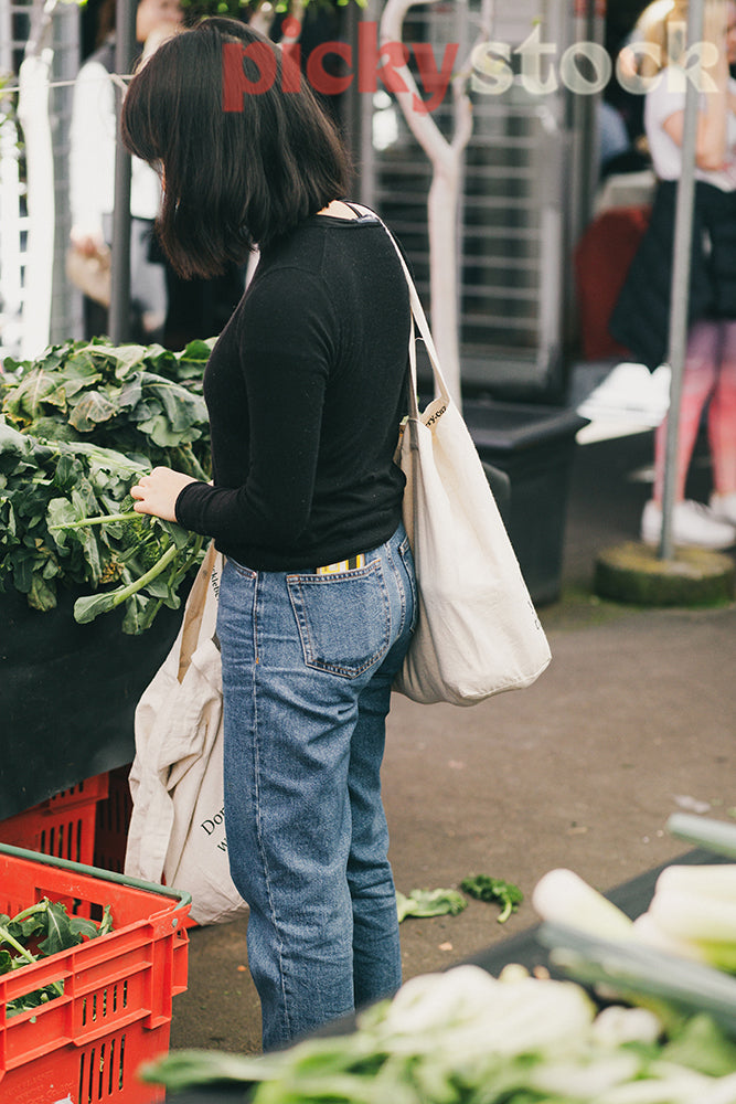 Young woman shopping for produce farmers market with reusable tote bags buying brocolli.
