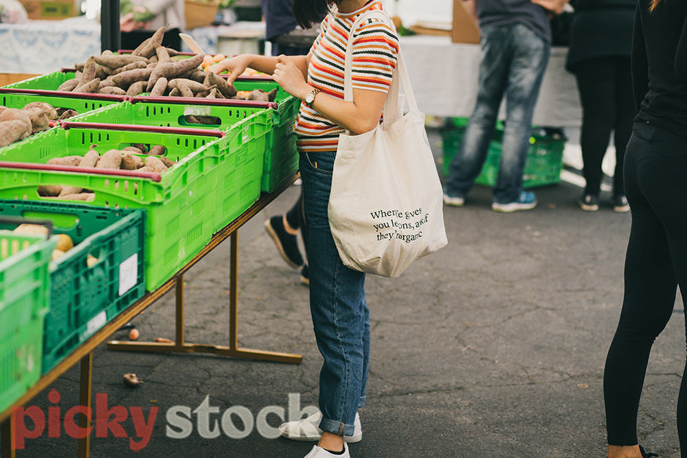 Young woman shopping for produce at farmers market standing in front of green crates.