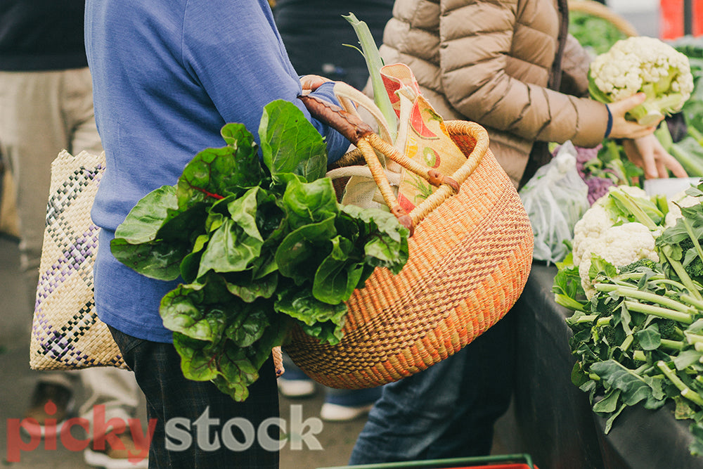 Woman at farmers market with woven basket buying vegetables.
