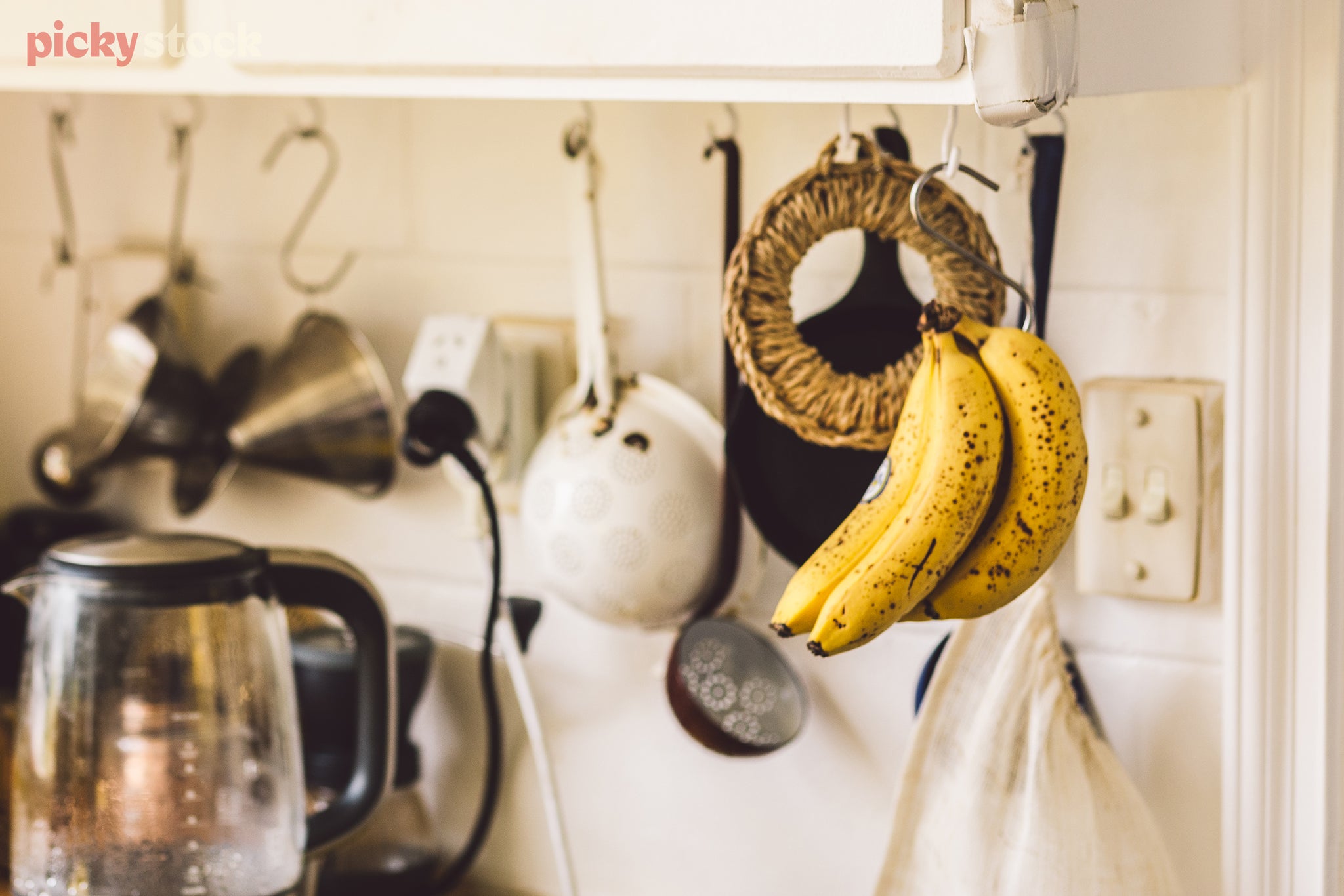 Nearly-over-ripe bananas hang in an Auckland kitchen, doused in sunlight. 