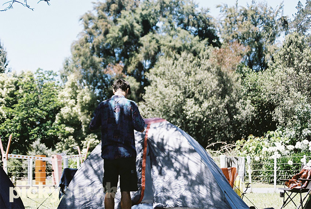 Young man sets up tent at campsite.