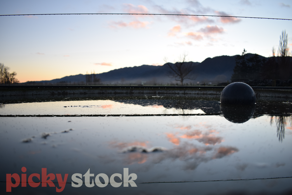 Reflection of the dawn sky in a frozen water trough on a farm