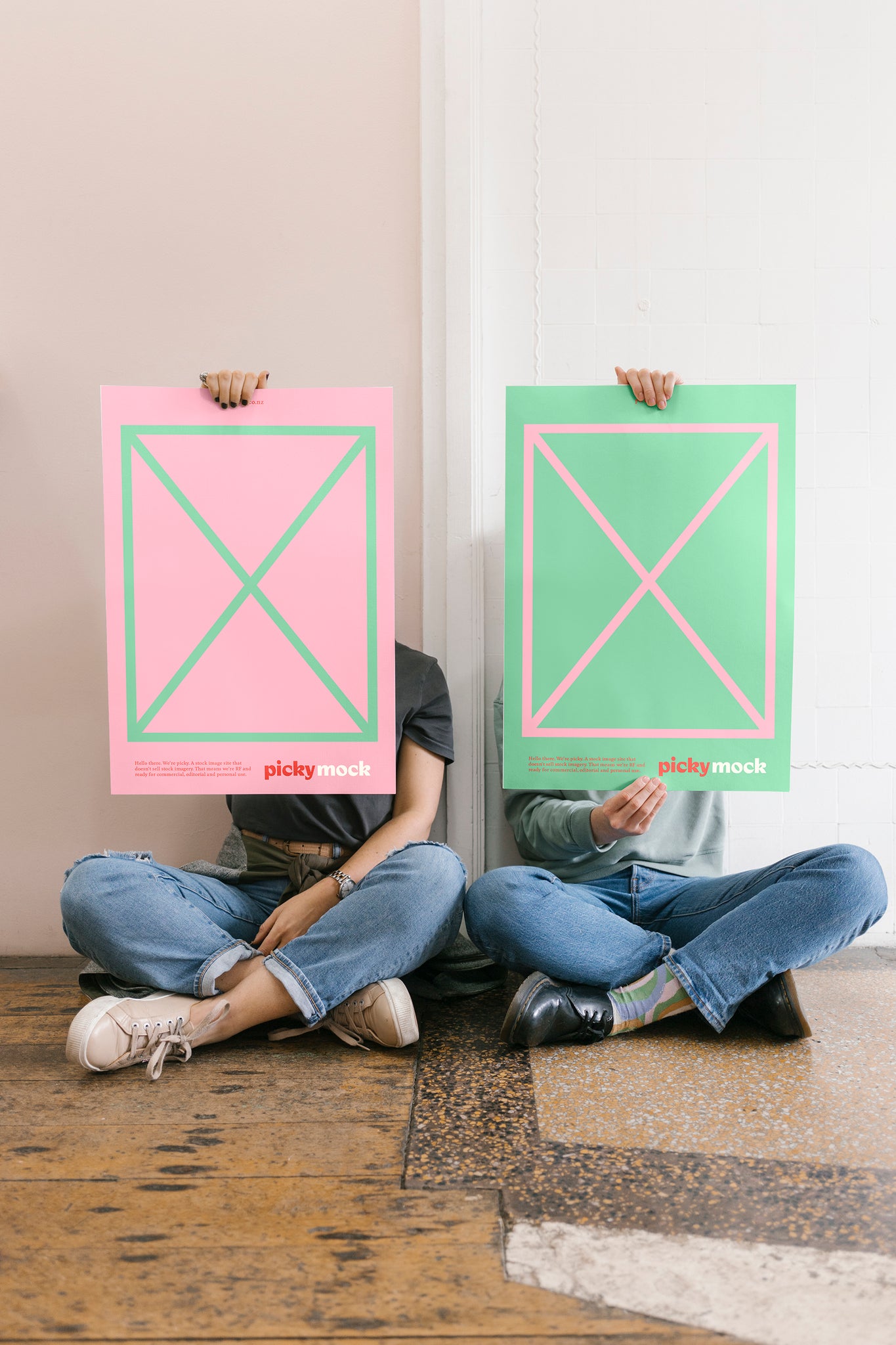 Portrait of two people sitting obscured by holding up mock advertisements in green and pink featuring small red picky logo.